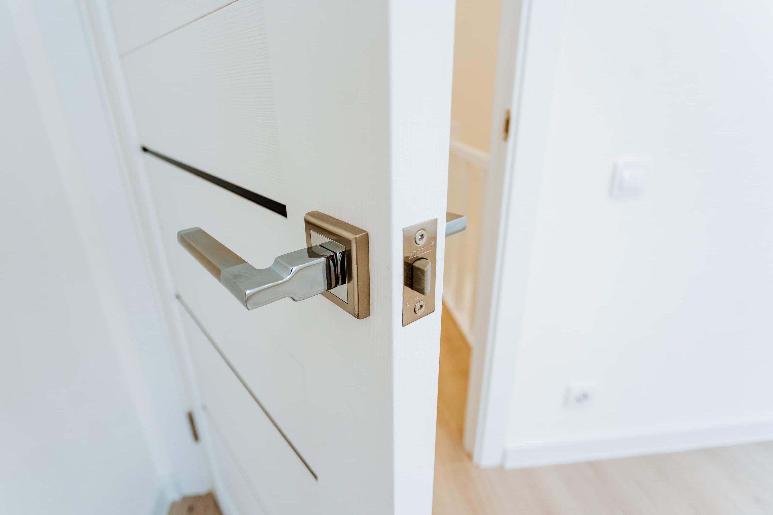 white door slightly open showing latch and chrome handle, closeup of lock mechanism and hinge, clean painted surface, and quality hardware, suitable for renovation, carpentry showcase, or real estate