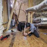 Two handyman installing flooring in an attic