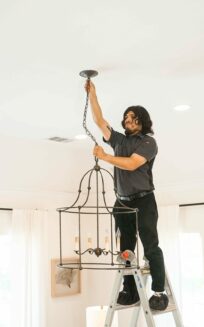 Technician on a ladder installing a light fixture in a white living room