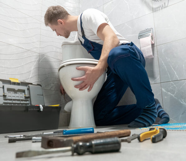 man plumber in uniform installing toilet