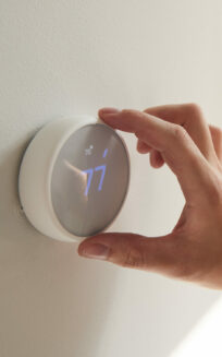 Close Up Of Male Hand Adjusting Digital Central Heating Thermostat In Home