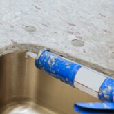 Caulk gun putting silicone sealant to installing a kitchen sink with modern decorative granite countertops